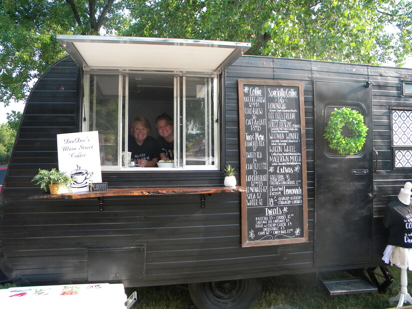 Owner of coffee trailer smiles through window, with employee.