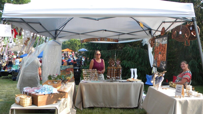 Vendors at outdoor market behind tables selling jewelry and gifts