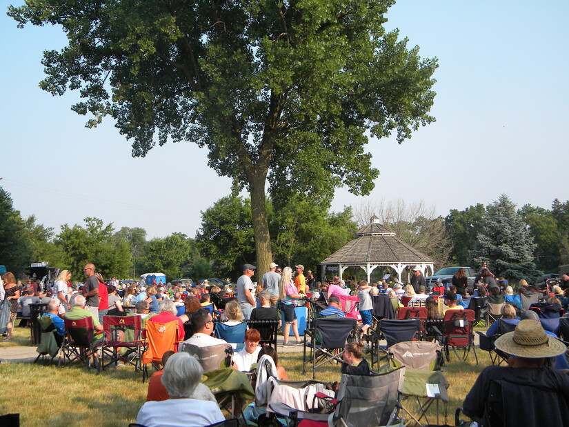 Visitors at summer outdoor market listen to live music at village park