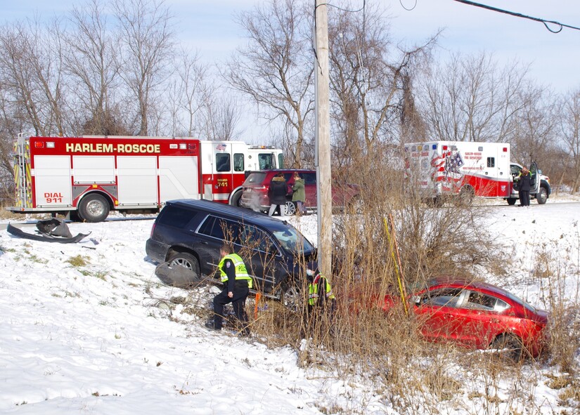Two cars in a ditch on a snowy day, with two fire department vehicles