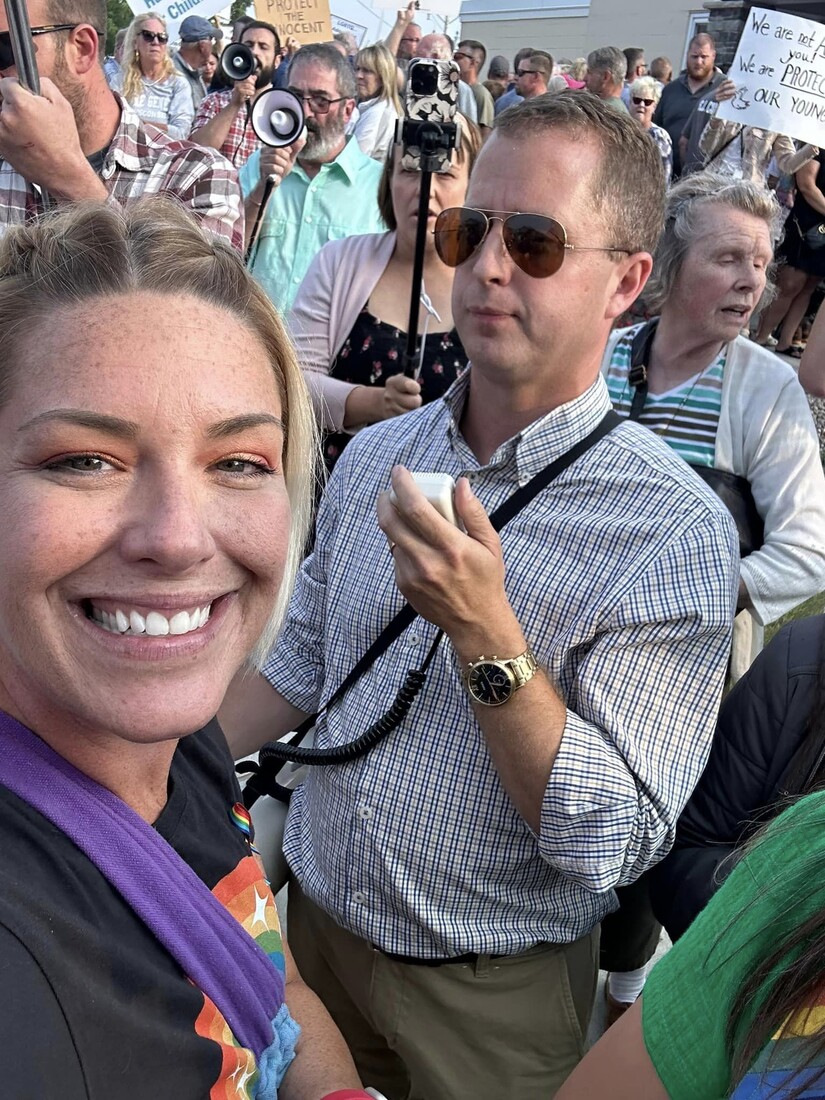 Woman smiles at camera while man in sunglasses ignores her during protests.