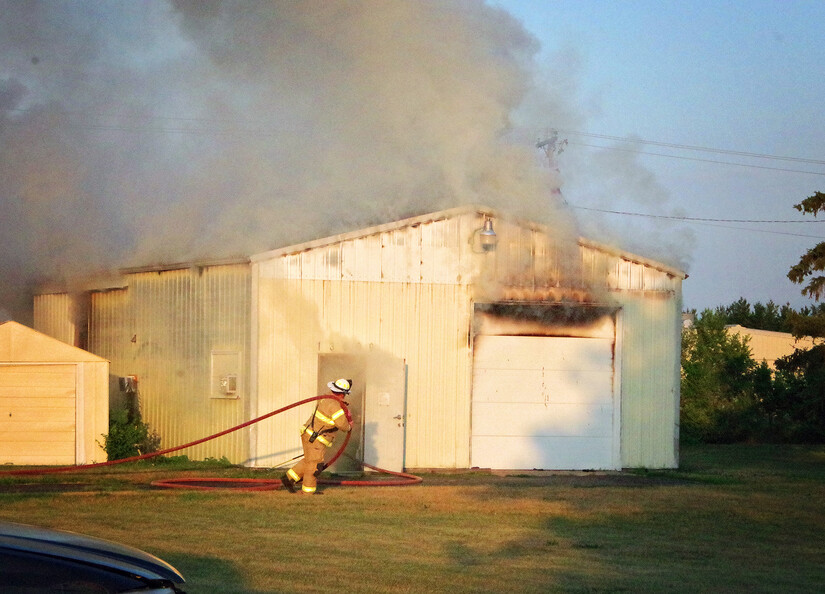 Smoke coming from metal building while firefighter drags hose to put out the fire.