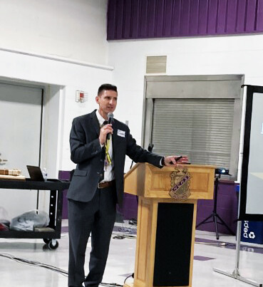 high school principal in gym with microphone and hand on lectern.