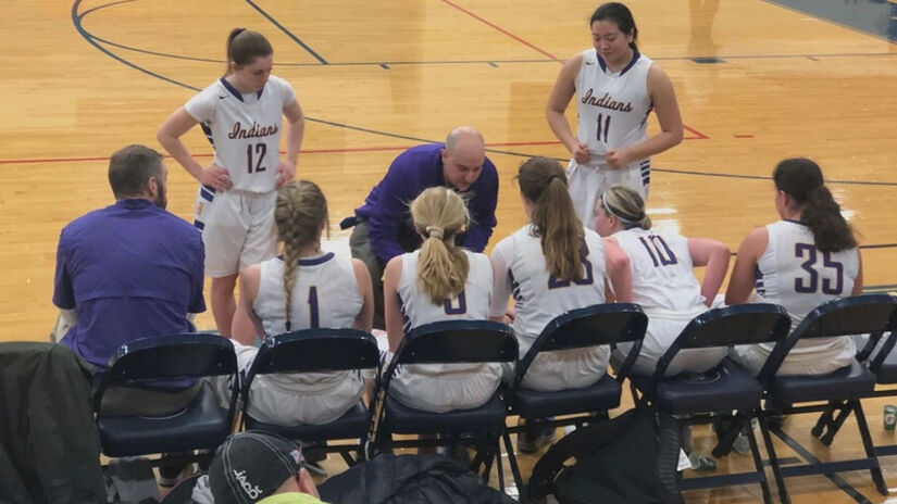 A girls basketball coach bends down to speak to his team on the bench.