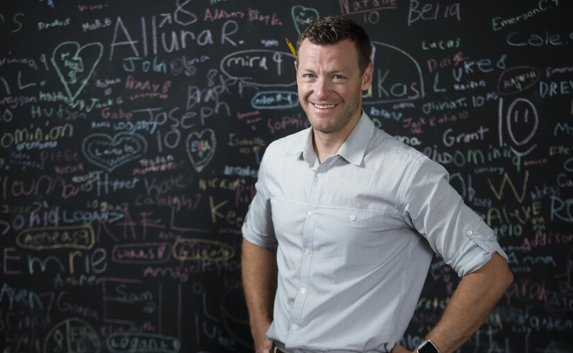 principal stands in front of chalkboard covered with names