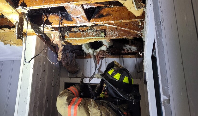 Firefighter digs up into attic after spraying foam.